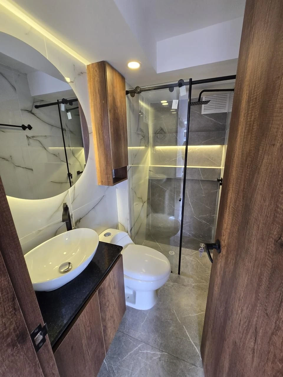 Baño en mármol con espejo circular LED y mampara negra