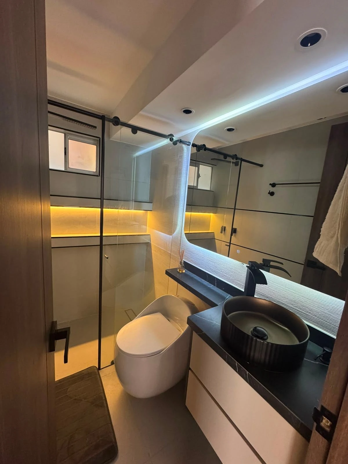 Baño con lavamanos negro, espejo LED y ducha de vidrio en Bogotá