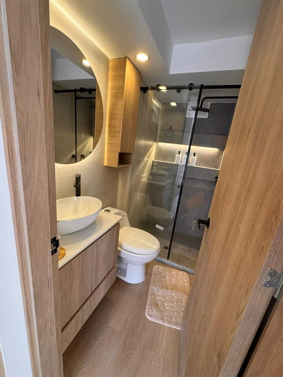 Baño en roble con espejo circular LED y mampara negra