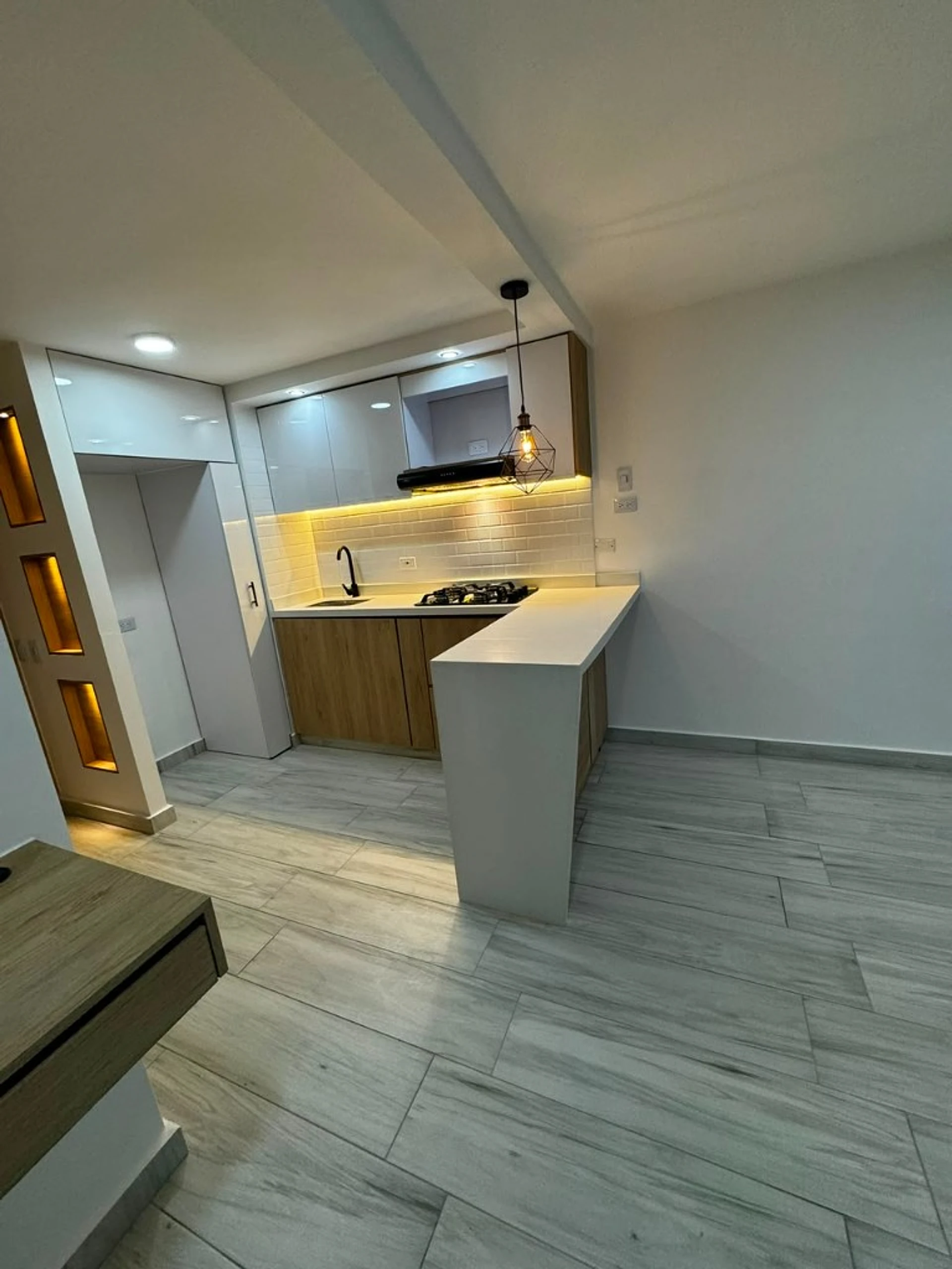 Cocina abierta con barra blanca, lámpara y LED bajo muebles