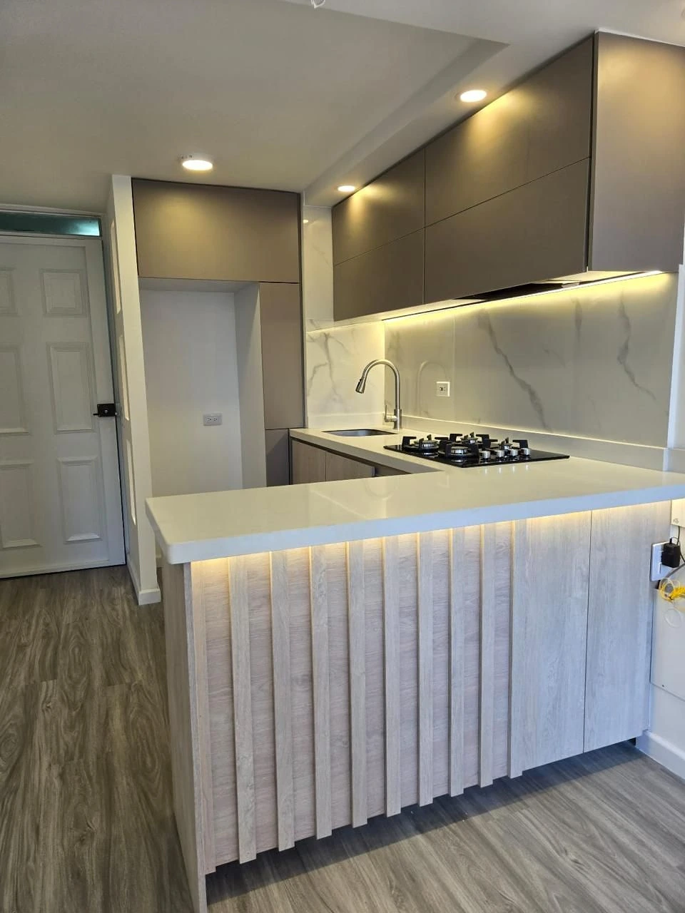 Cocina con barra listonada, LED y cubierta blanca en Bogotá