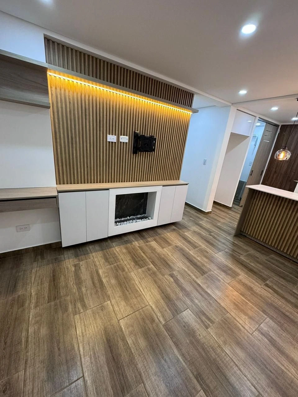 Sala con panel listonado, chimenea y cocina abierta al fondo