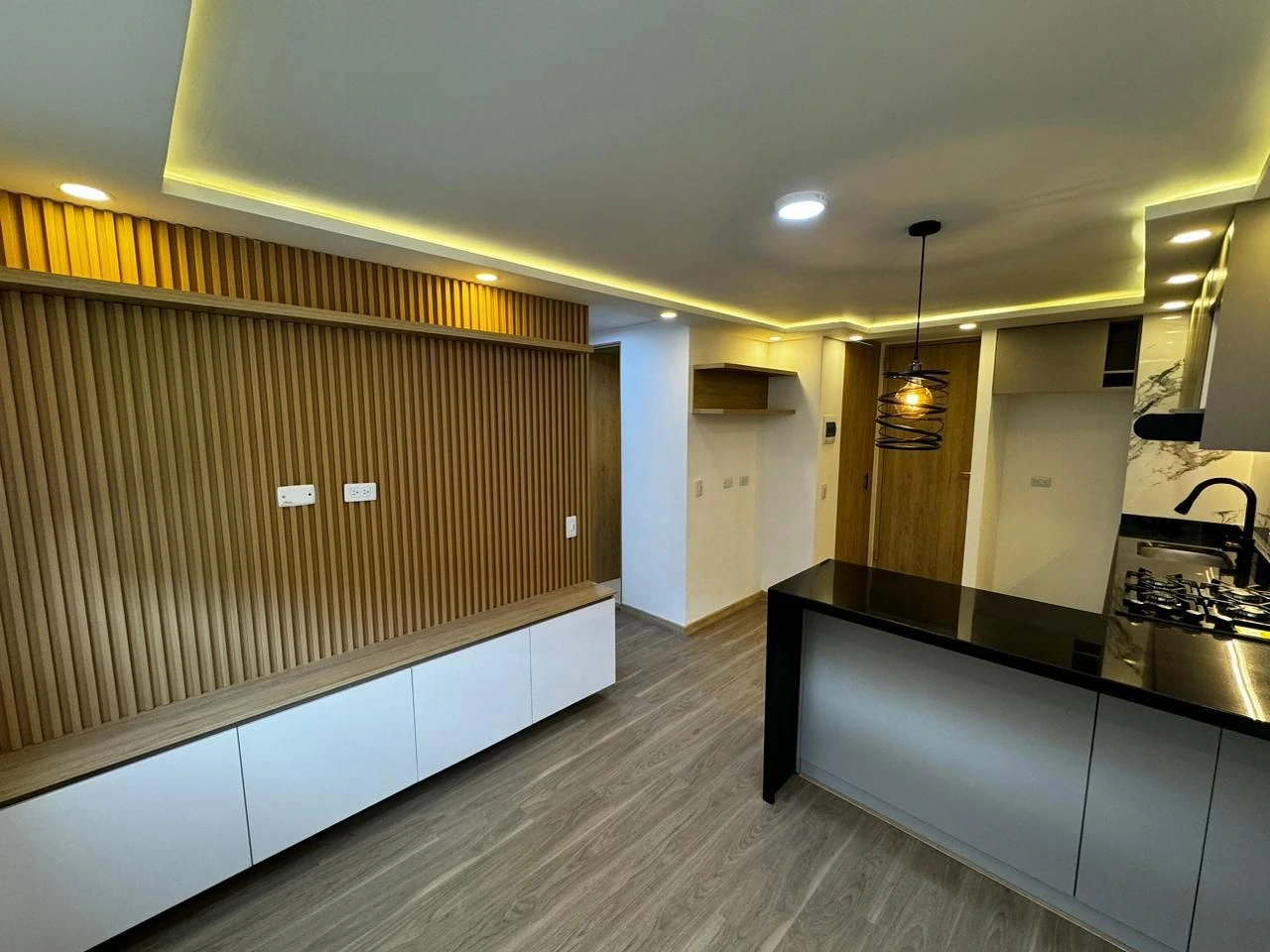 Sala y cocina abiertas con panel listonado, barra negra y LED